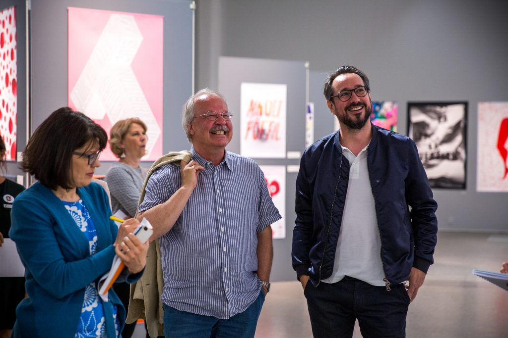 People standing in row smiling in a tall room, which has posters on its walls.