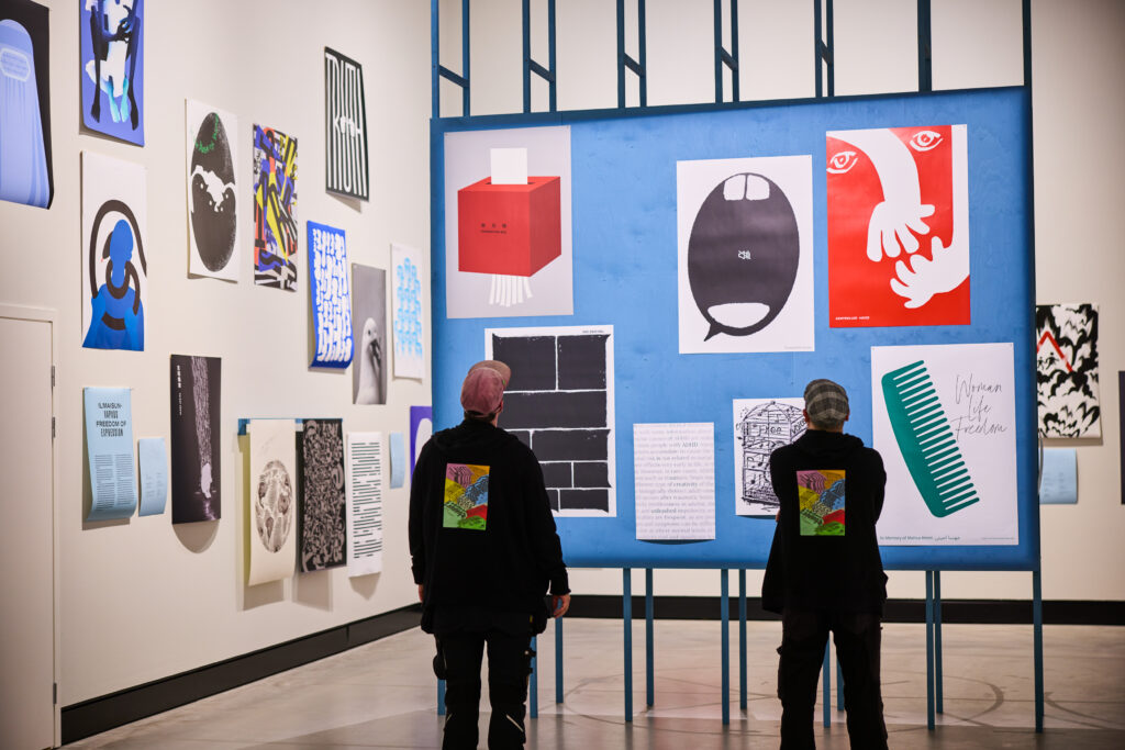 Kaksi henkilöä katselee julisteita näyttelytilassa.