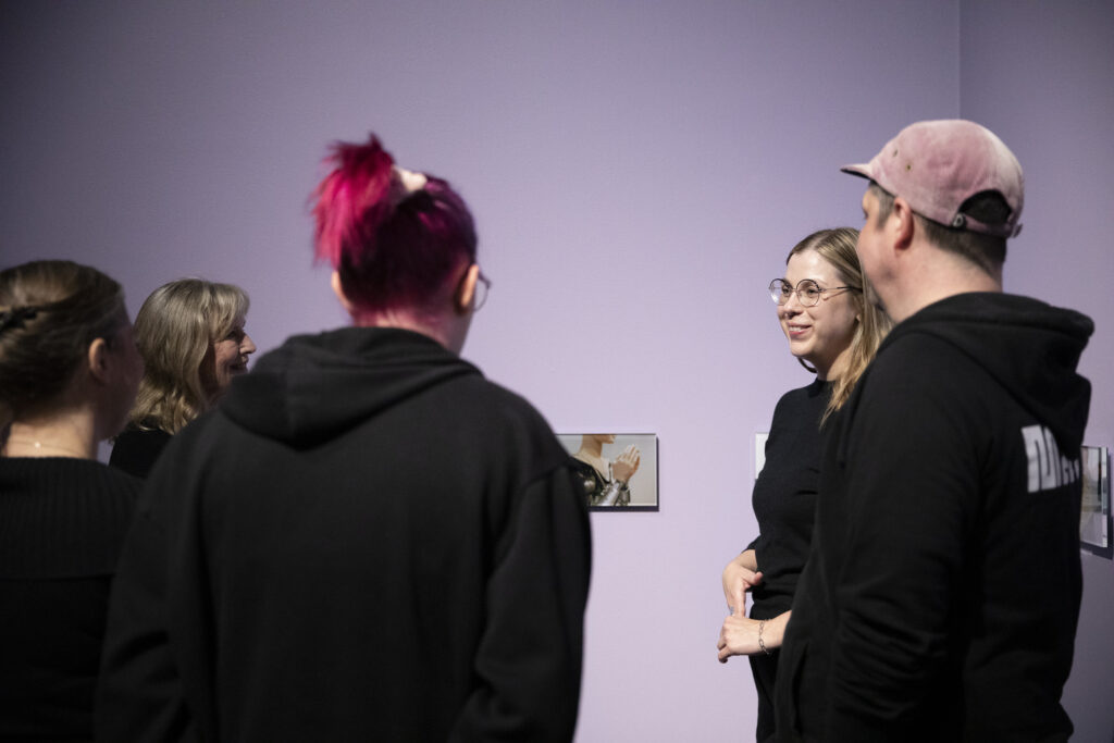 Henkilöitä keskustelemassa Outo vetoima -näyttelyssä.