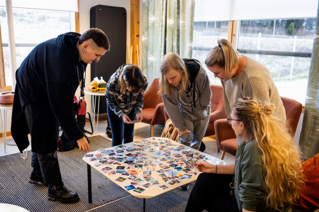 viisi henkilöä pöydän ääressä katsomassa valokuvia.