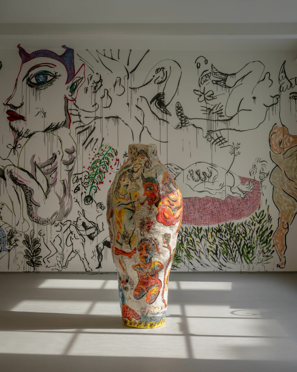 Kussa on keskellä iso ruukku, jossa värikkäitä kuvia ja taustalla seinällä isoja hahmoja ja kasveja.