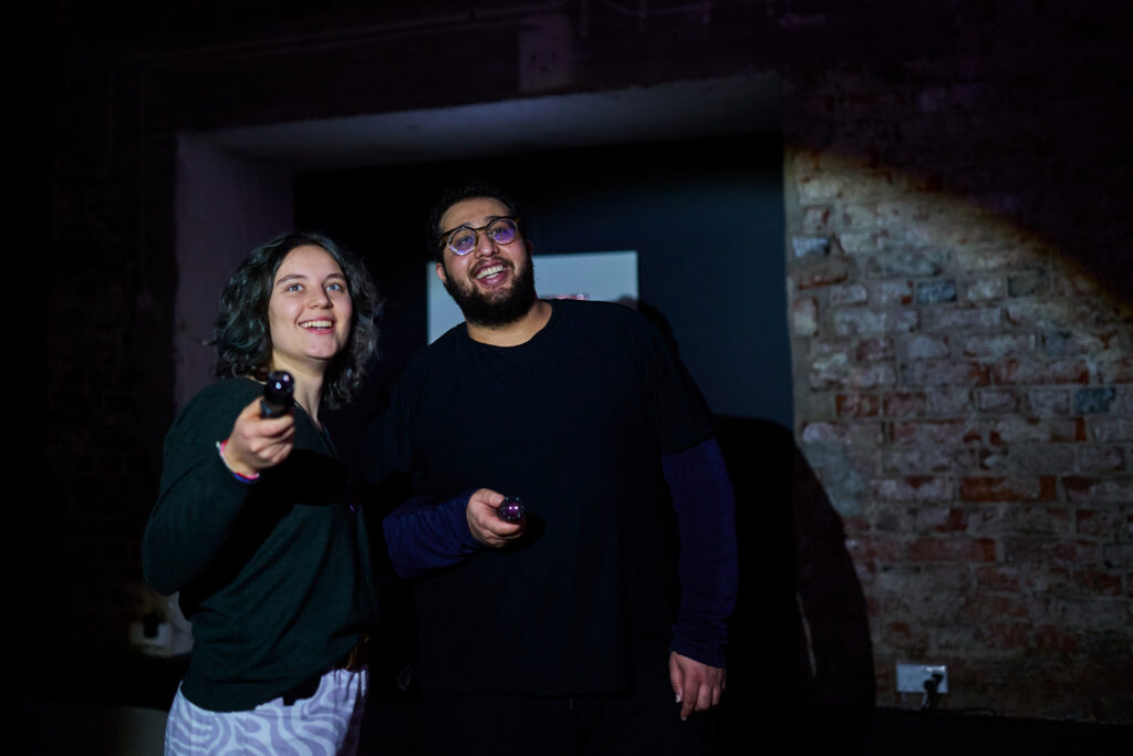 Kaksi henkilöä osoittaa taskulampuilla teosta.