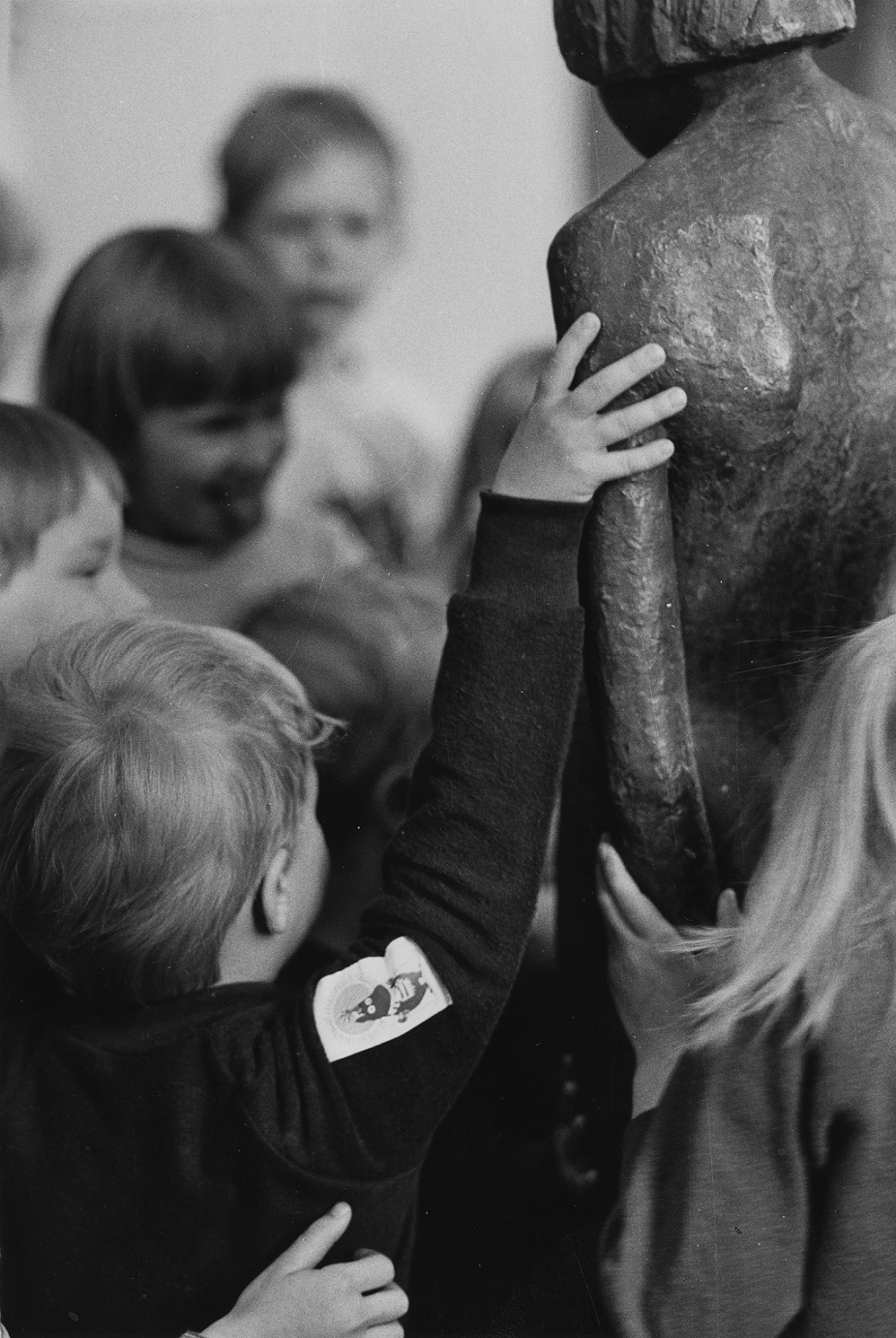 A child reaching to touch the shoulder of a sculpture representing a person.