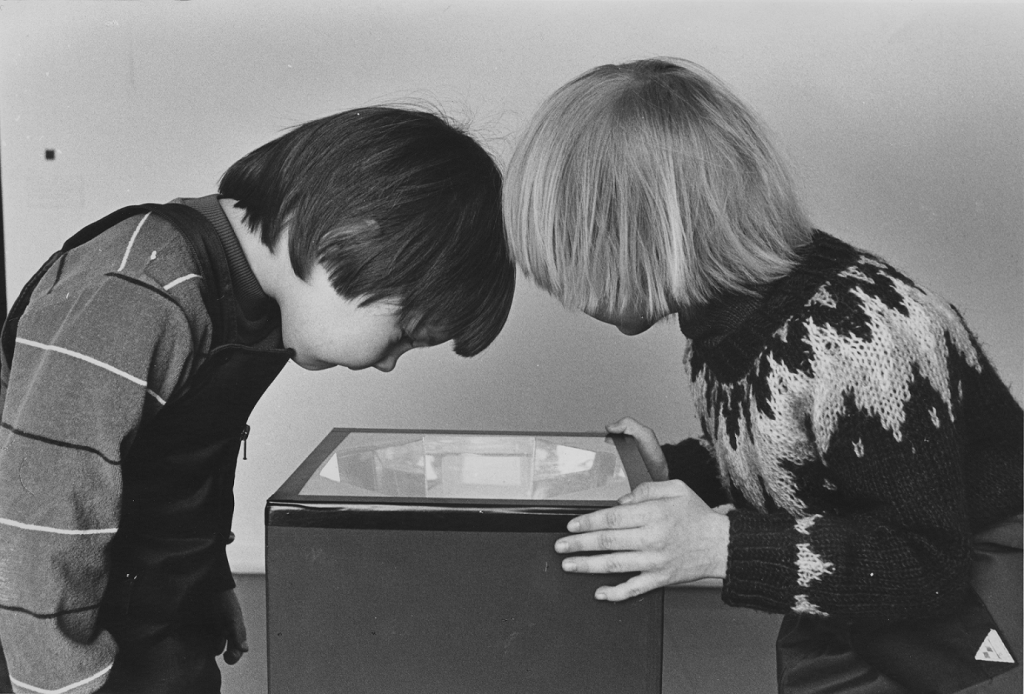 Two children in an old photo, peeking into a box from the above.